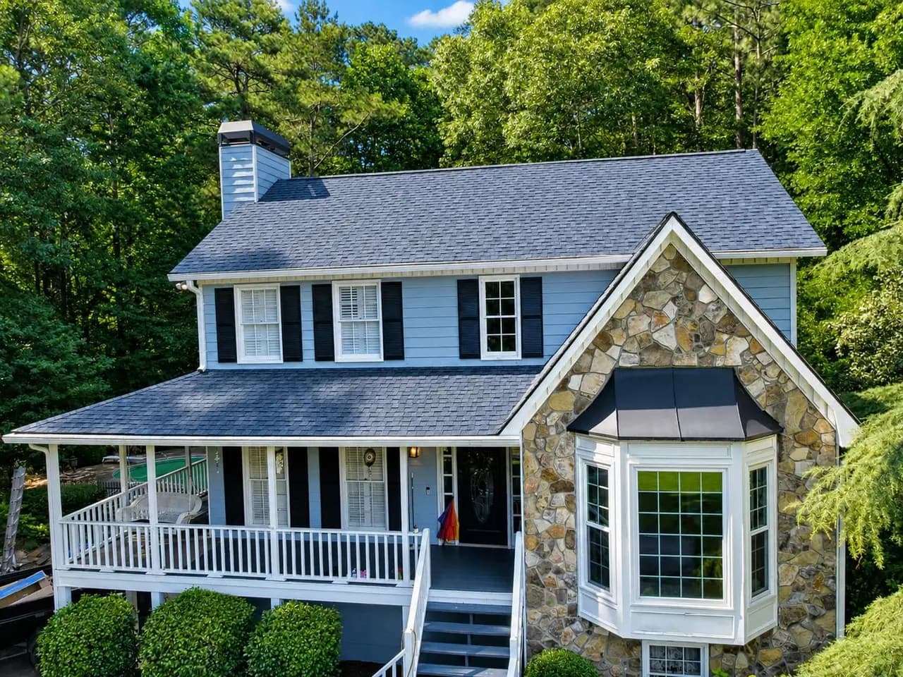 A two-story blue colonial home with a stone gable, a covered front porch, and a new charcoal architectural shingle roof installed by Platinum Roofing