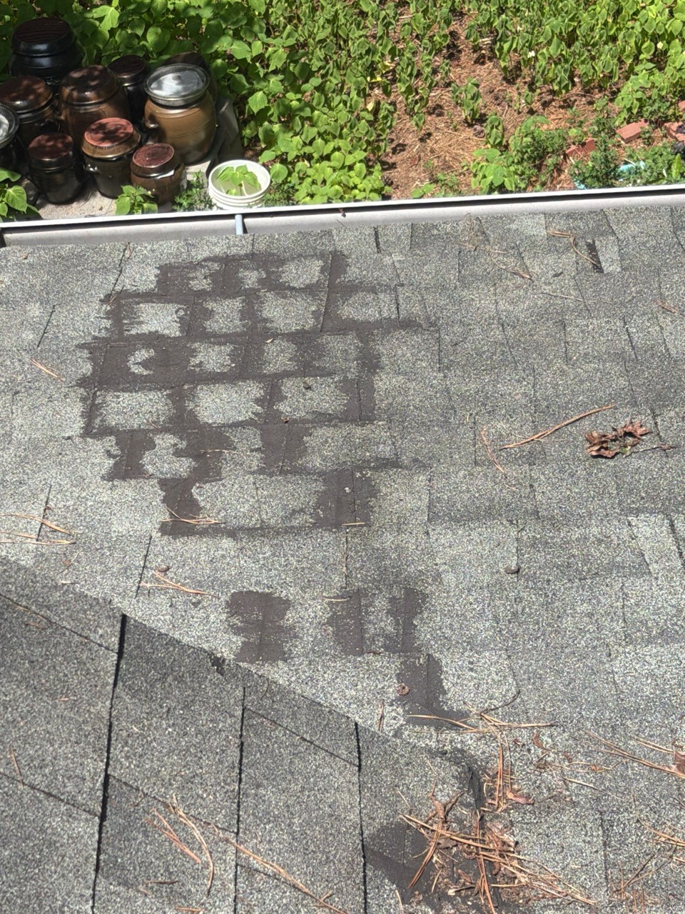 Dark, uneven patches across an aging asphalt shingle roof near the gutter line
