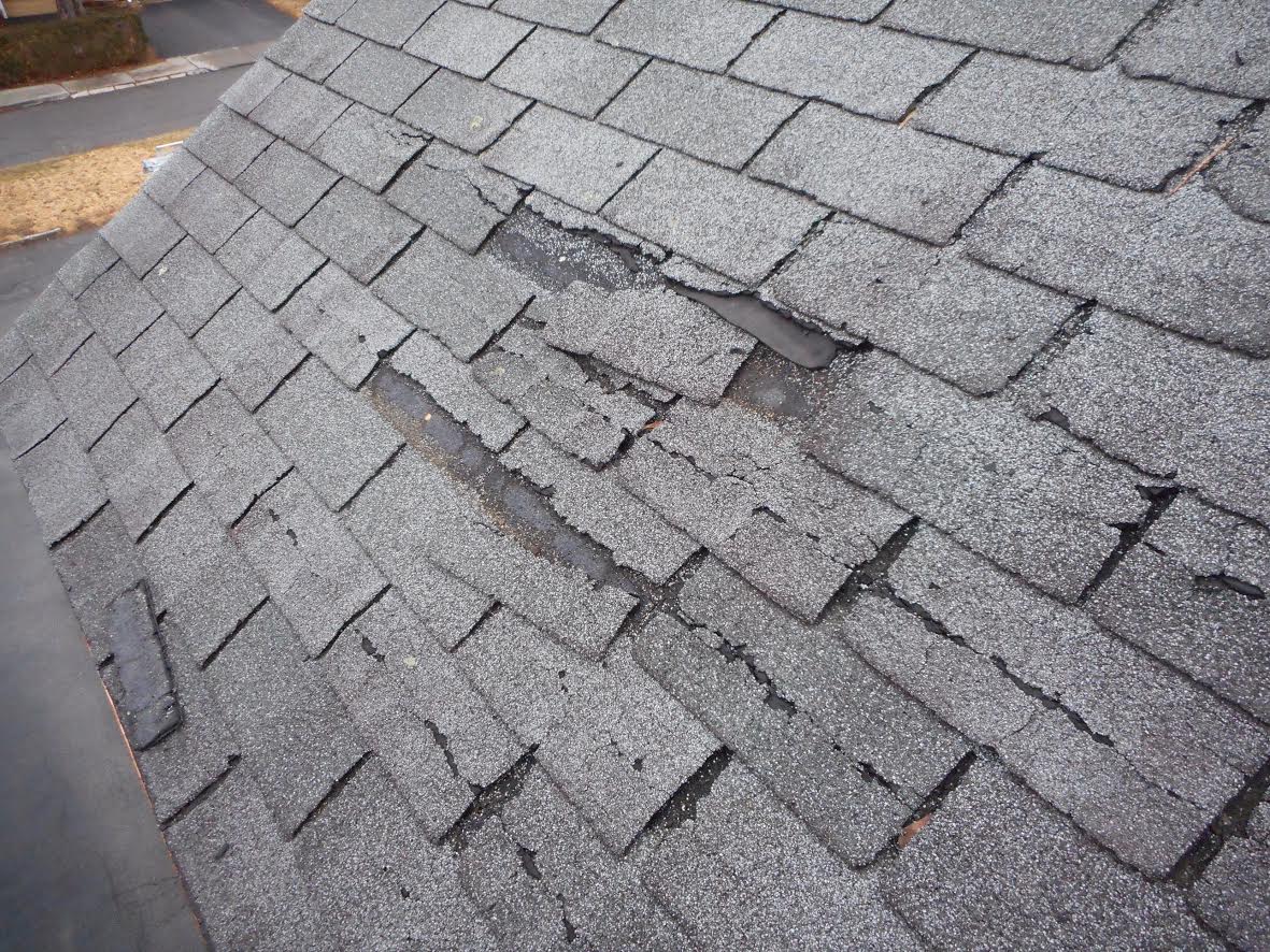 A close-up of asphalt shingles that are cracked and worn with the protective granules knocked off