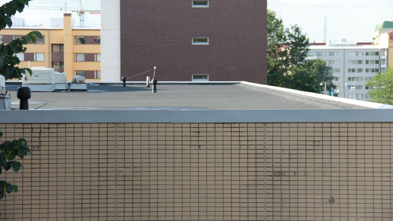 A dark modified-bitumen felt membrane on a low-slope commercial roof with metal edge flashing and vent penetrations