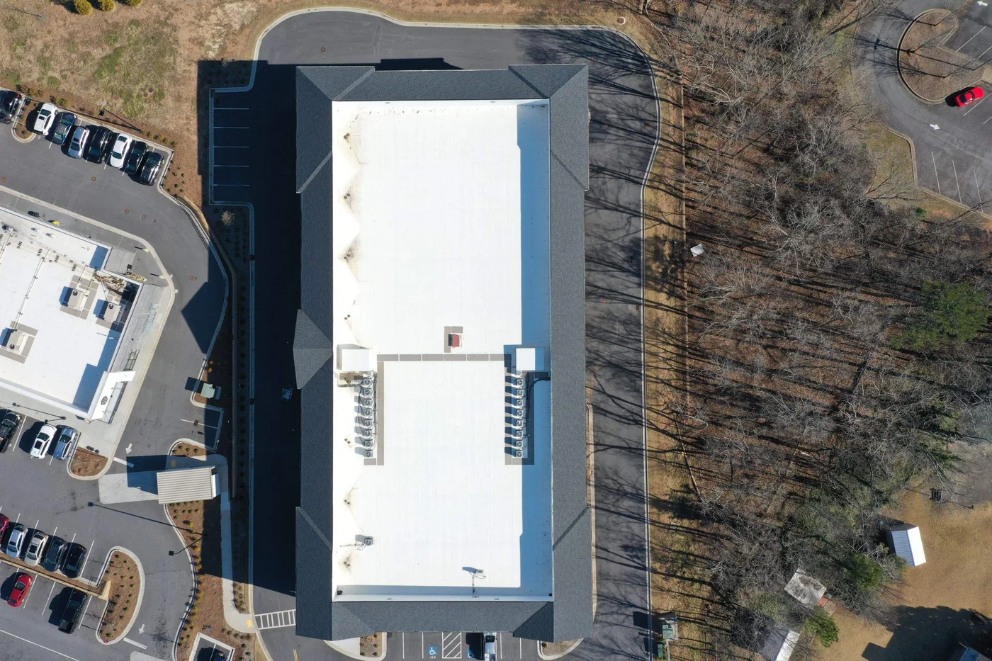 Top-down aerial of a commercial office building with a white membrane roof surrounded by a shingle mansard, showing rooftop HVAC units and penetrations serviced by Platinum Roofing