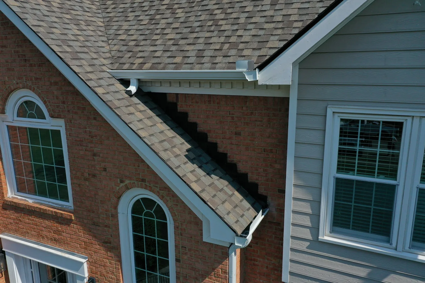 Seamless white gutter and downspout wrapping the roof edge of a brick North Atlanta home