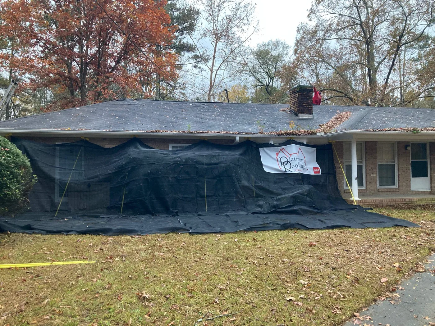 A North Georgia home with protective tarps draped over the landscaping and porch during a Platinum Roofing tear-off, with the company banner displayed